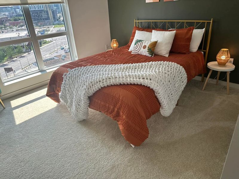 Airbnb bedroom with a freshly made bed, rust throw, and city-view window after a Sparkling Haven turnover