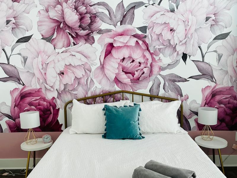 Bedroom with floral accent wall, white bedding, and rolled towels ready for check-in